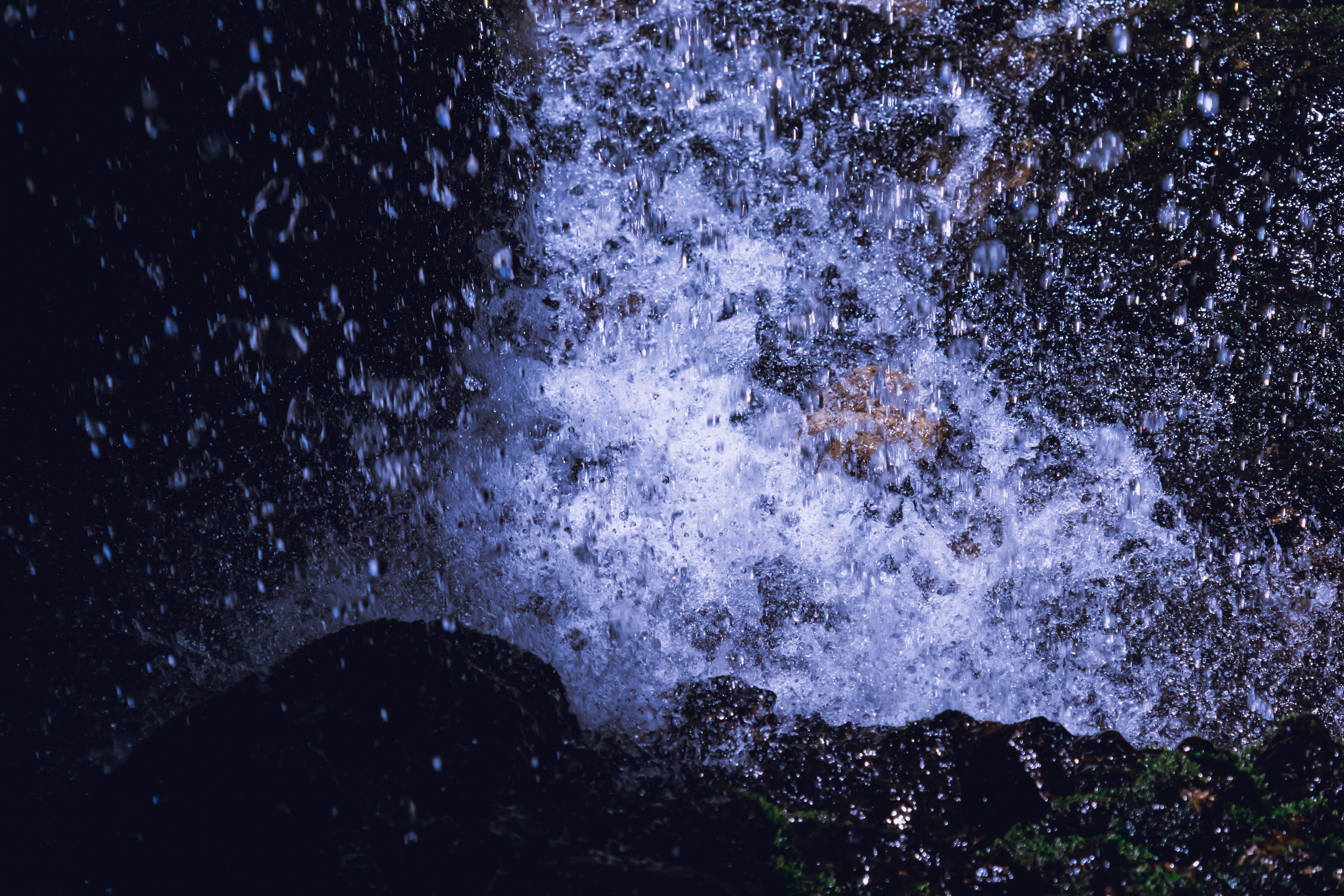 Backlit water splash, fine droplets against dark rock