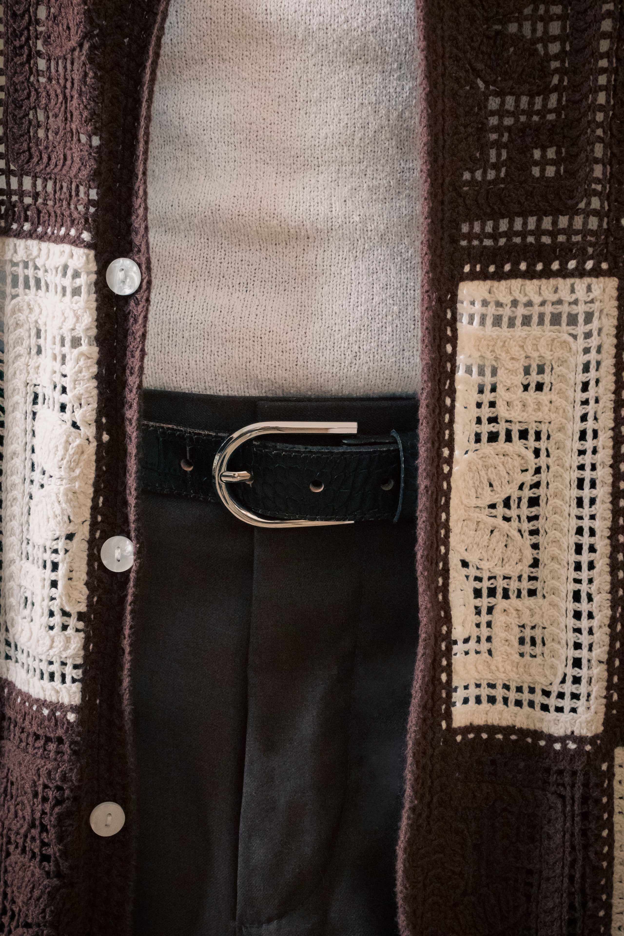 Crochet cardigan over knit top with leather belt close-up