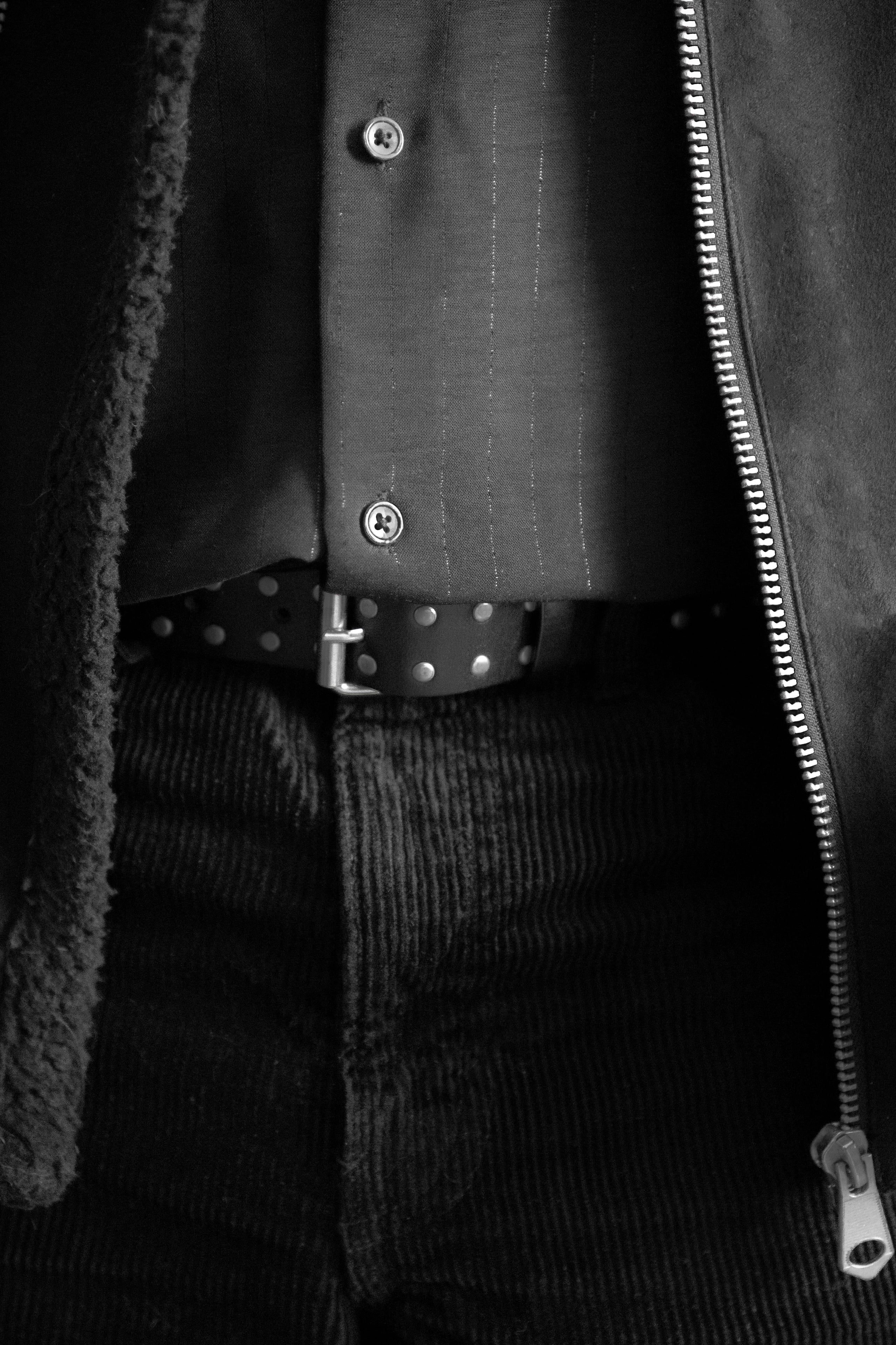 Black-and-white close-up of zipped jacket, striped shirt, studded belt and corduroy pants